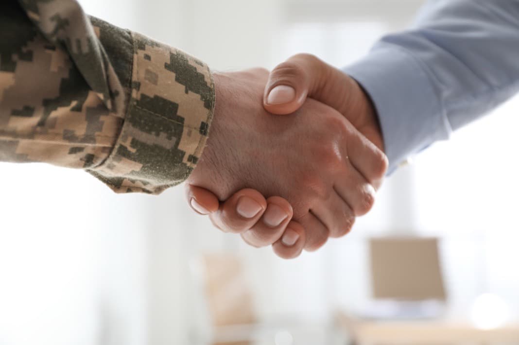 A service member in uniform shaking hands with a business partner